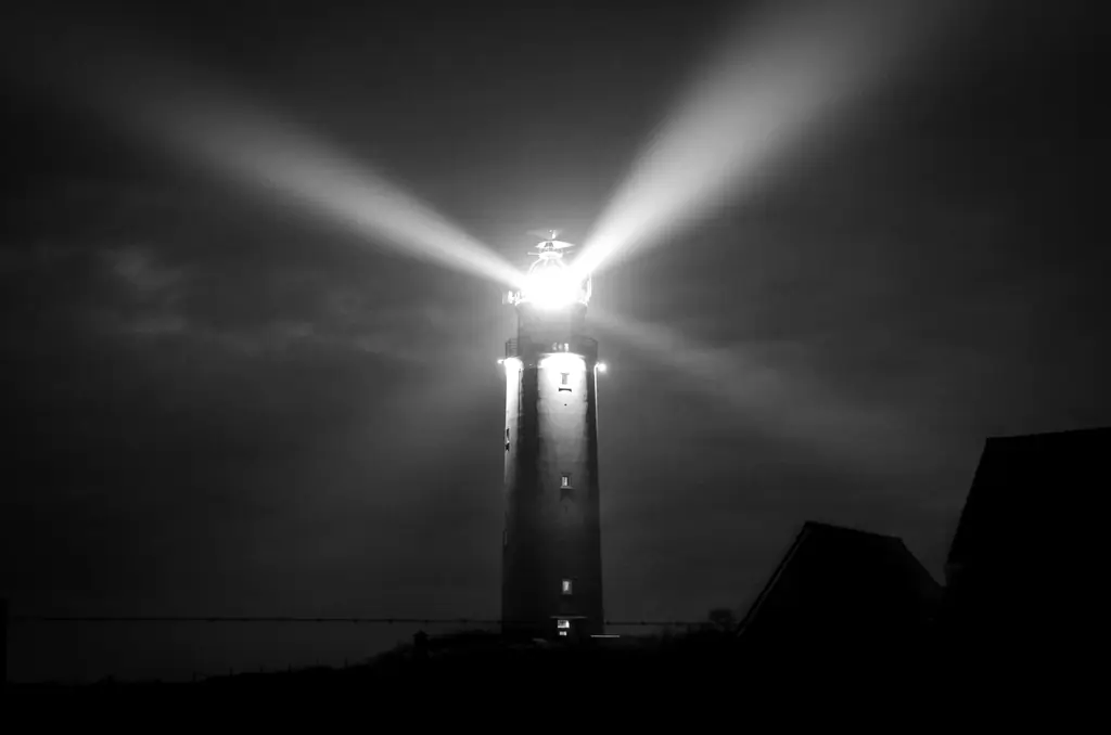 Um farol aceso na noite, com feixes de luz cortando o escuro.